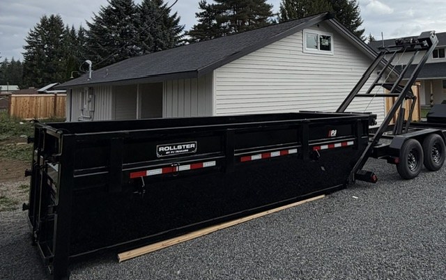 Black roll-off dumpster on trailer beside a home
